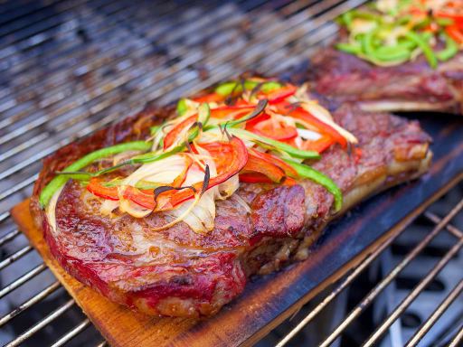 Gegrilde Ribeye steak met pepers en uien op cederhout